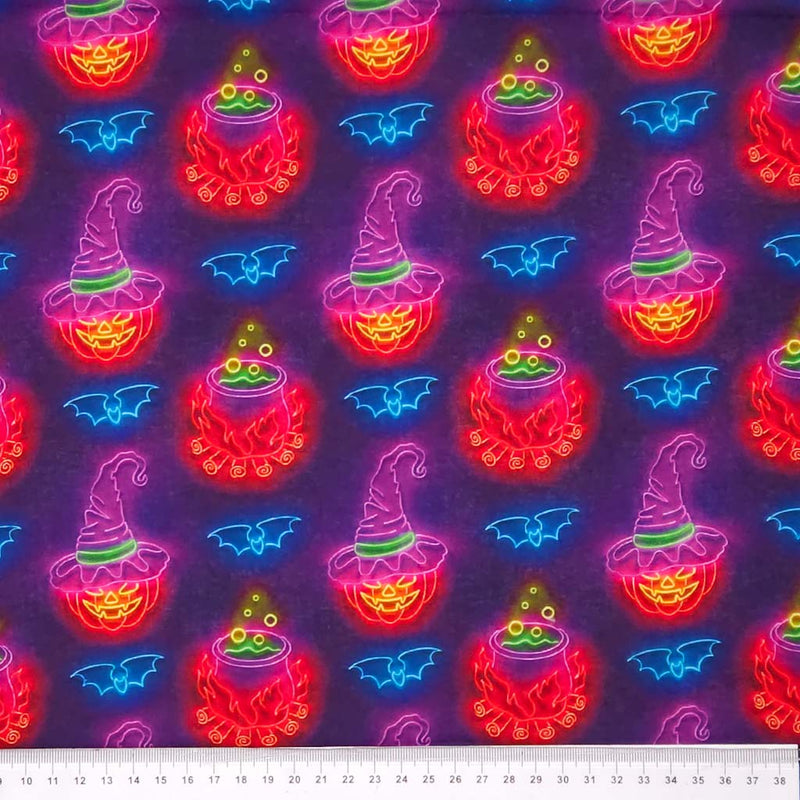 Neon Halloween-themed fabric pattern with pumpkins, cauldrons, and bats on a dark cotton fabric with a cm ruler.