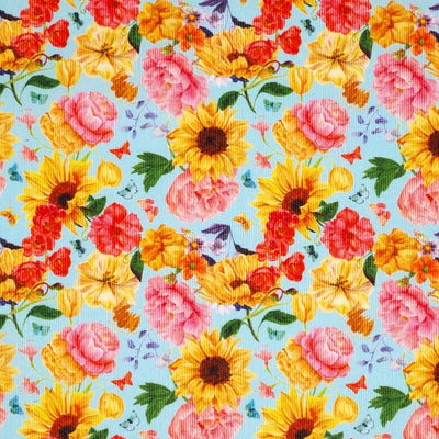Bright sunflowers and pink roses are printed on a sky blue needlecord fabric