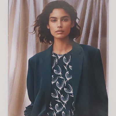 Woman wearing a dark blue blazer over a patterned shirt with a neutral background
