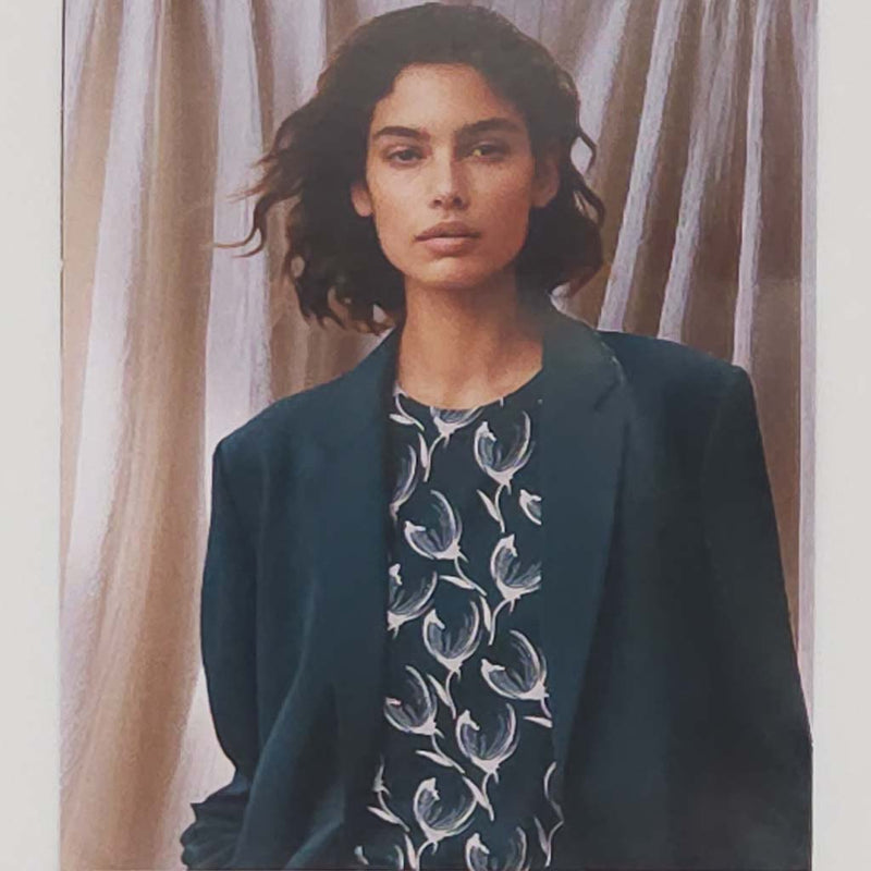 Woman wearing a dark blue blazer over a patterned shirt with a neutral background