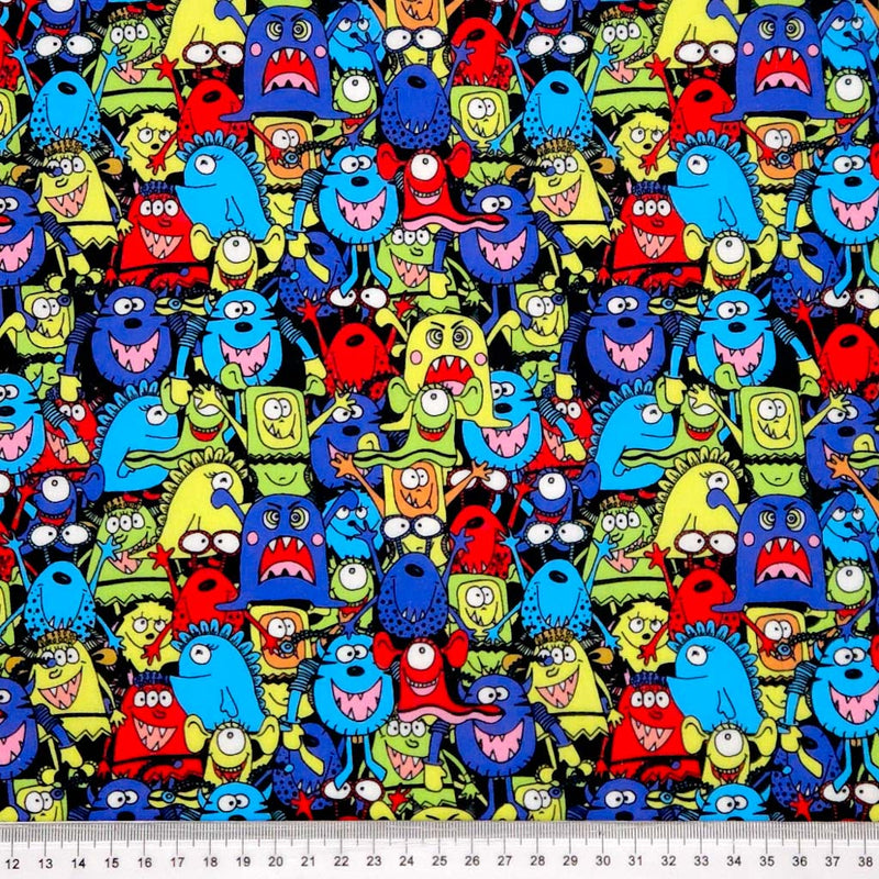 Pattern of colorful cartoon monsters on a black halloween polycotton fabric with a ruler at the bottom.