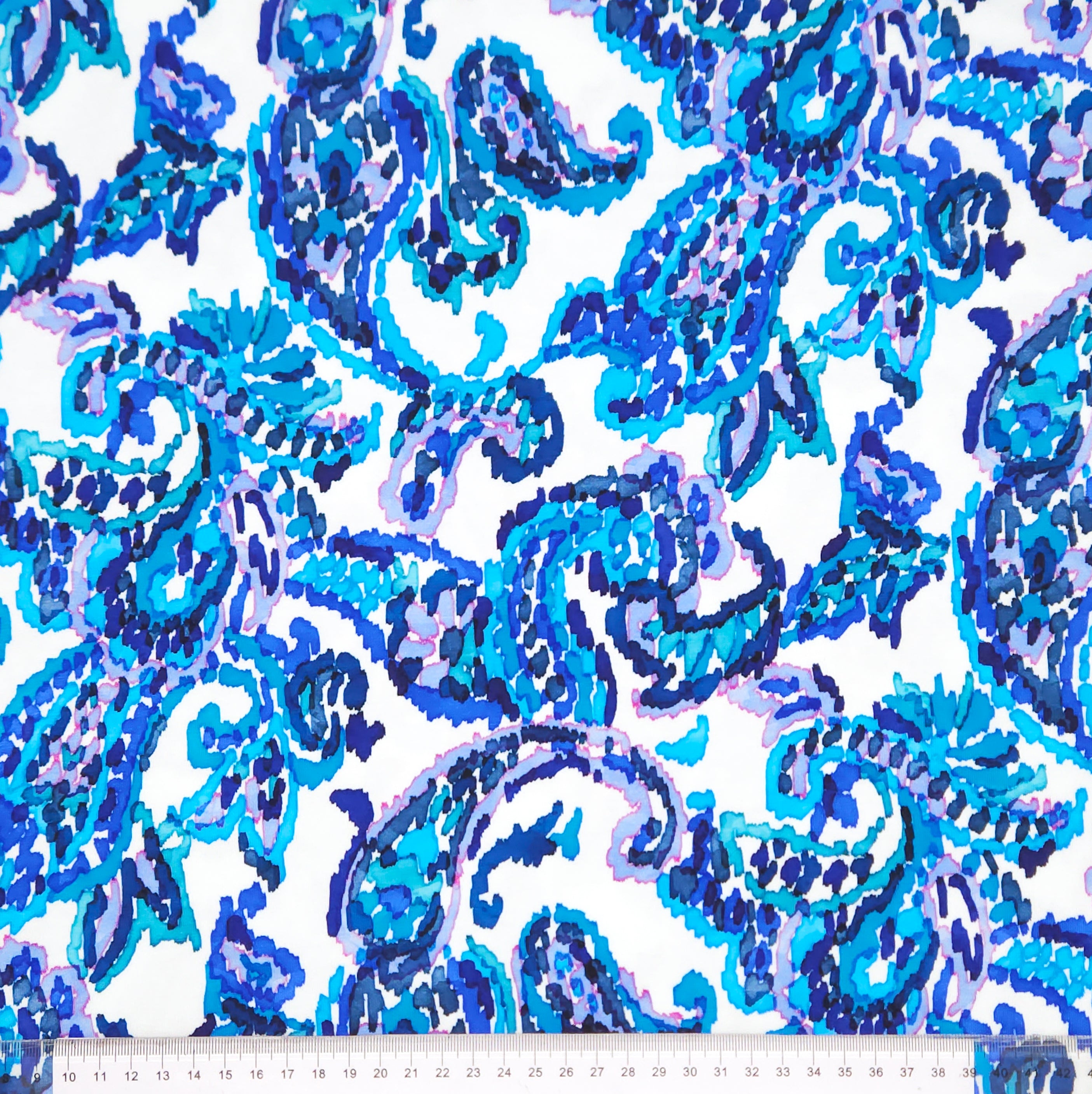 A blue paisley design printed on a white cotton jersey fabric with a cm ruler