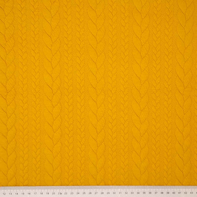A plain mustard coloured cable knit dressmaking fabric with a cm ruler