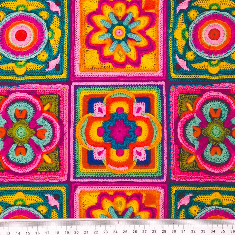 Colourful crocheted squares with floral patterns on a cotton fabric with a cm ruler