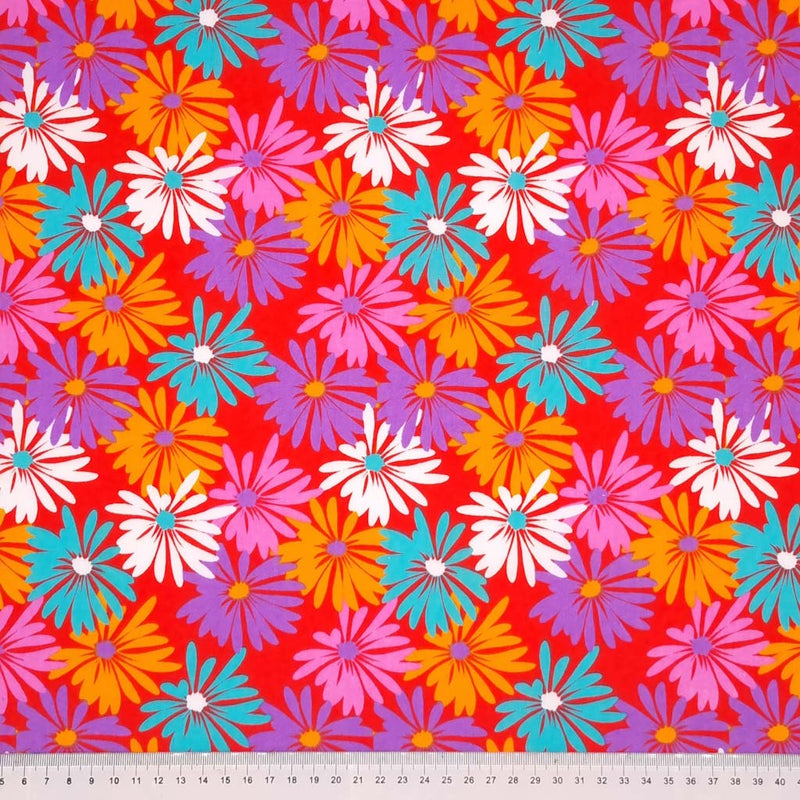 Pretty white, blue and orange spring daisies are printed on a red polycotton fabric with a cm ruler