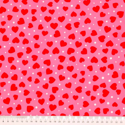 Red ditsy hearts printed on a pink polycotton fabric with a cm ruler