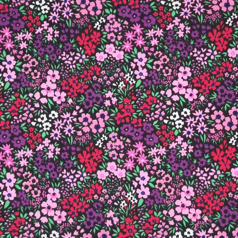 Ditsy flowers in pinks and purples are printed on a black polycotton fabric