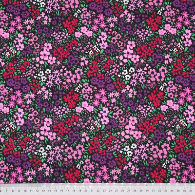 Ditsy flowers in pinks and purples are printed on a black polycotton fabric with a cm ruler