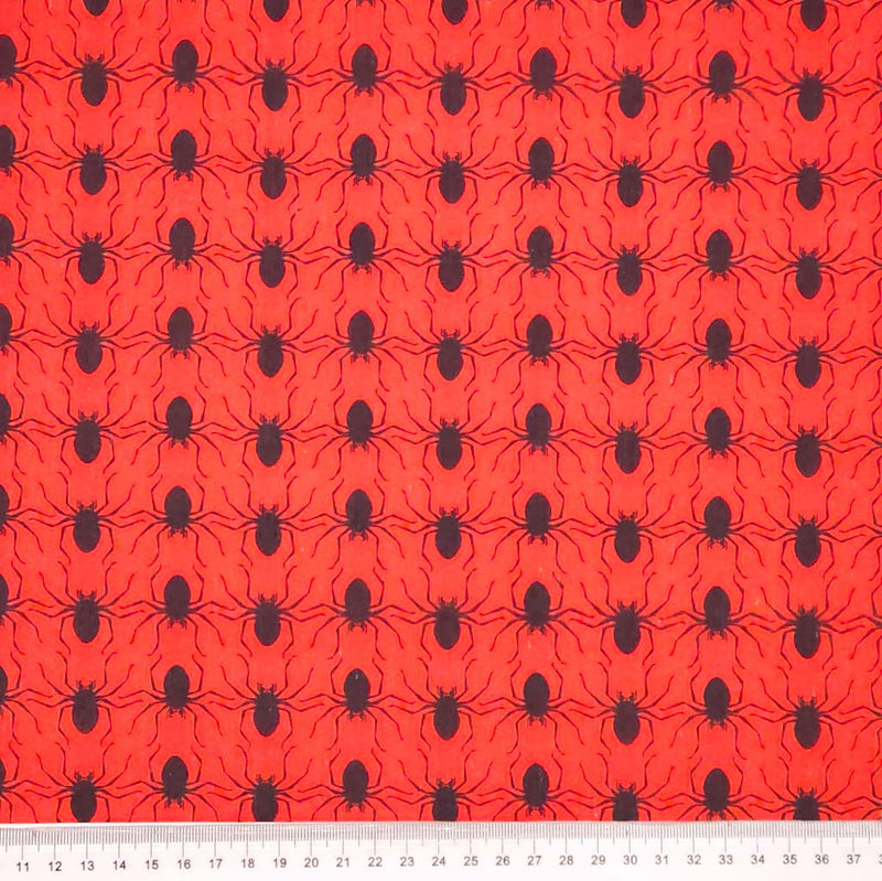 Red halloween polycotton fabric with black spider pattern and a ruler at the bottom for scale.