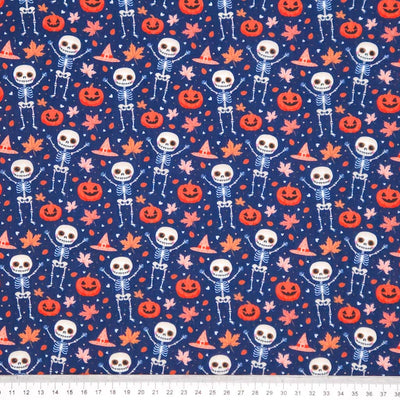 Pattern of skeletons, pumpkins, and leaves on an indigo halloween polycotton fabric with a cm ruler