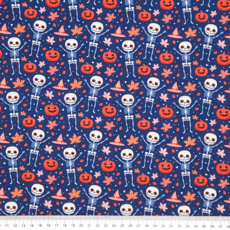Pattern of skeletons, pumpkins, and leaves on an indigo halloween polycotton fabric with a cm ruler