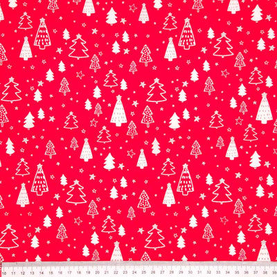 Pattern of white Christmas trees and stars on a red cotton fabric with a ruler