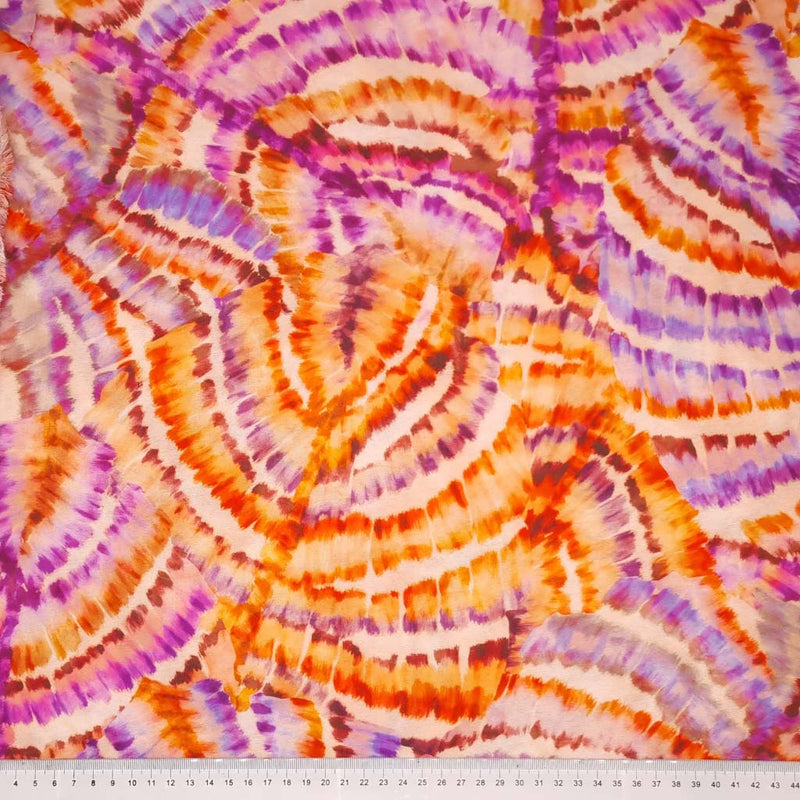 Purple and orange tie dye wheels are printed on a viscose fabric with a cm ruler