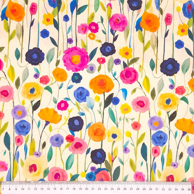 A floral viscose featuring delicately painted multicoloured wildflowers on a light cream dressmaking fabric with a cm ruler