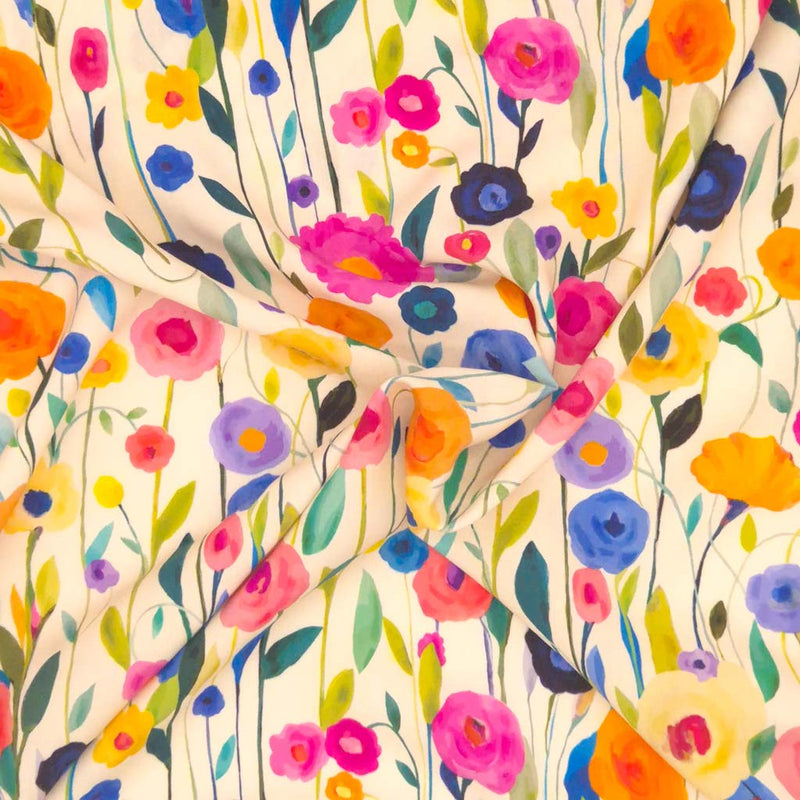 A floral viscose featuring delicately painted multicoloured wildflowers on a light cream dressmaking fabric in a swirl