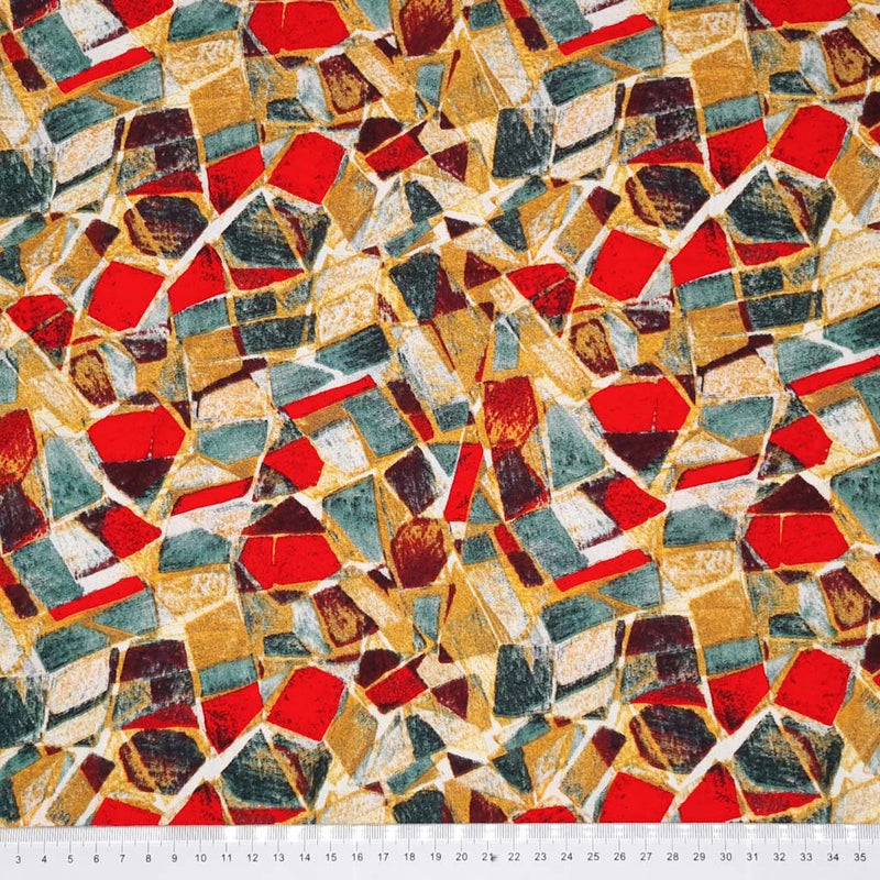 An abstract mosaic print on a woven viscose fabric in reds and teals with a cm ruler