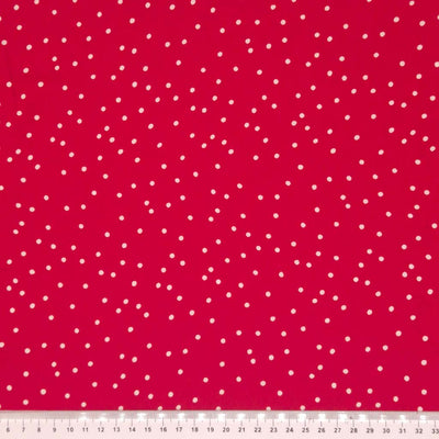 Small scattered white spots printed on red viscose fabric with a cm ruler.