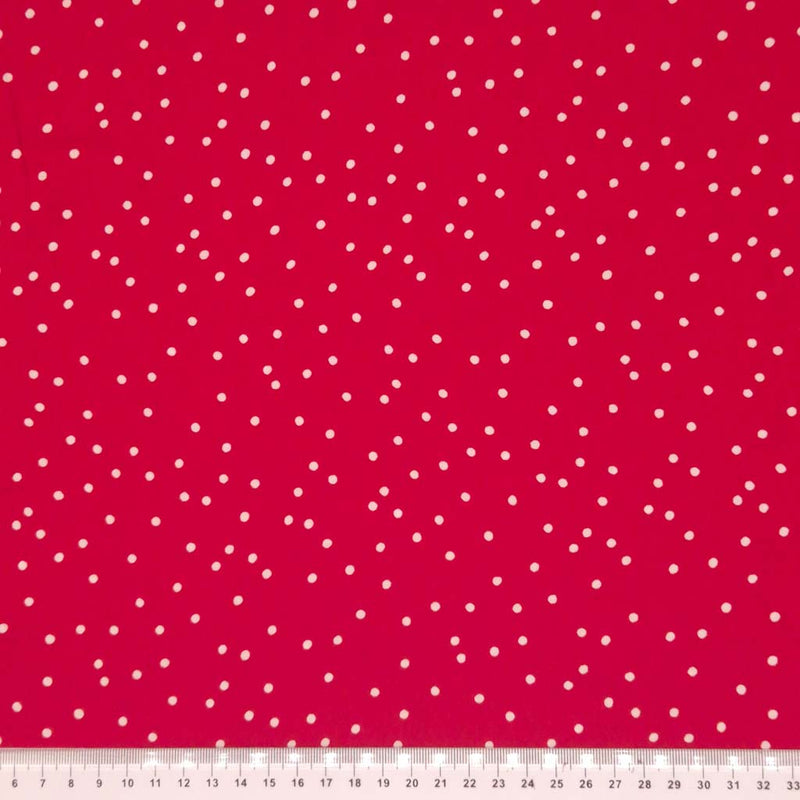 Small scattered white spots printed on red viscose fabric with a cm ruler.