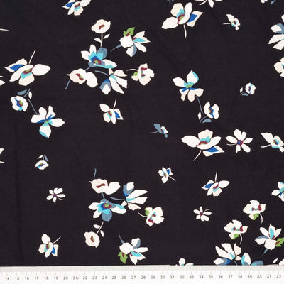 A white floral with sky blue detail is printed on a black viscose fabric with a cm ruler