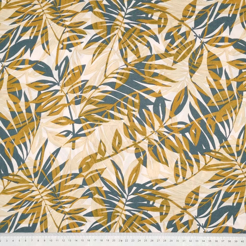 Teal and golden tropical leaves are printed on an ivory viscose dressmaking fabric with a cm ruler