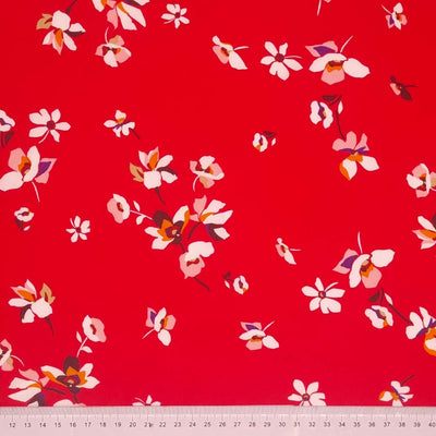 White flowers are printed on a red viscose fabric with a cm ruler