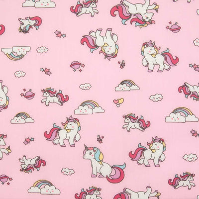 Cute white unicorns, colourful rainbows and stars are printed on a pink polycotton fabric