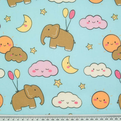 Blue elephants, pink and yellow balloons with orange sunshine and yellow moons printed on a sky blue polycotton fabric with a ruler for size perspective