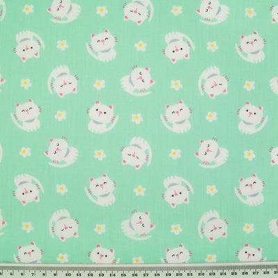 White cats with little daisies are printed on a mint polycotton fabric with a ruler at the bottom for size perspective