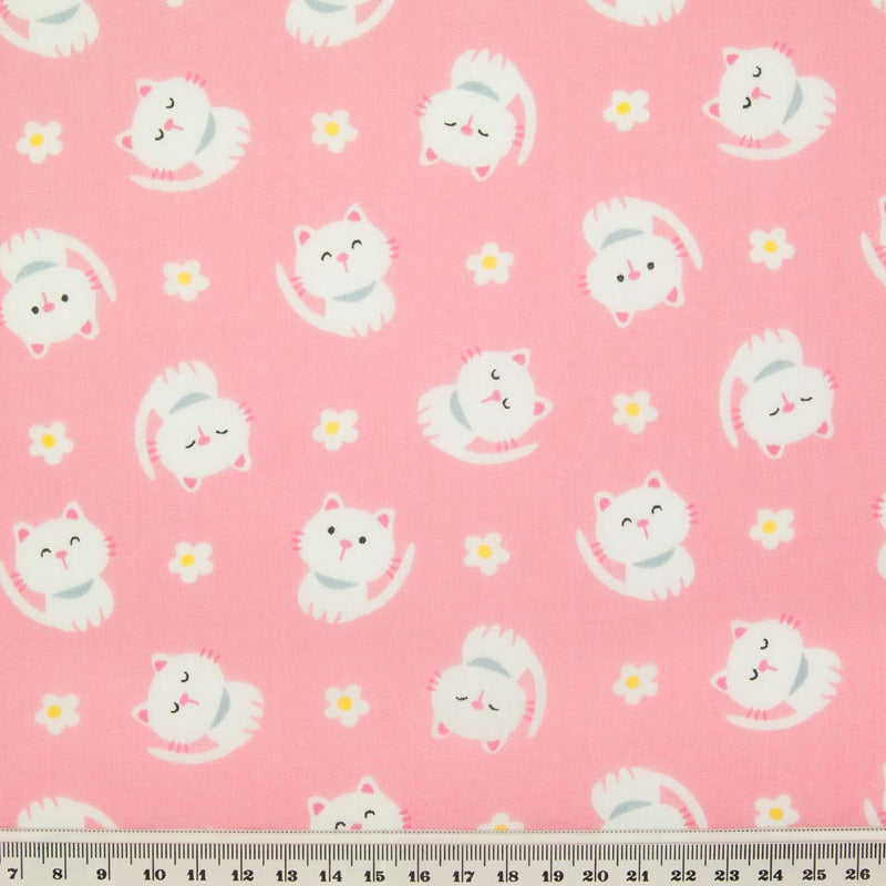 White cats with little daisies are printed on a pink polycotton fabric with a ruler at the bottom for size perspective