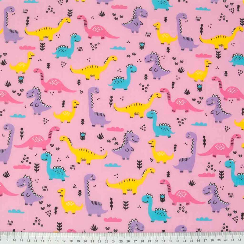 Yellow, pink and lilac happy dinosaurs printed on a pink polycotton fabric with a cm ruler at the bottom
