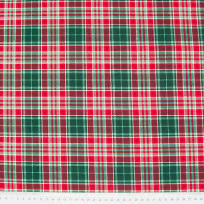 A 100% cotton christmas tartan plaid fabric with a dominant colour of forest green and red with a cm ruler at the bottom
