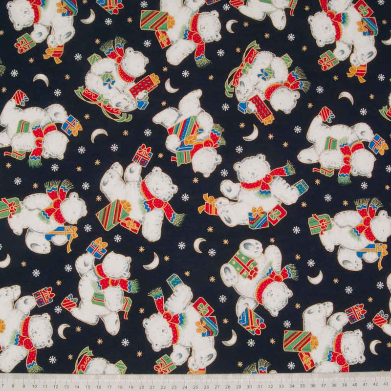 Festive teddies holding christmas gifts are printed on a navy 100% cotton fabric by Rose & Hubble with a cm ruler at the bottom