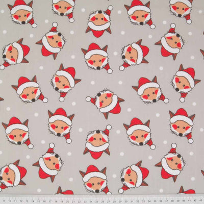 Cheeky fox faces wearing santa hats are printed on a silver polycotton christmas fabric with a cm ruler at the bottom