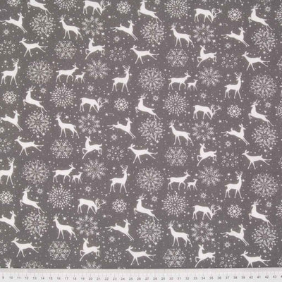 White reindeer and snowflakes are printed on a grey christmas polycotton fabric with a cm ruler at the bottom