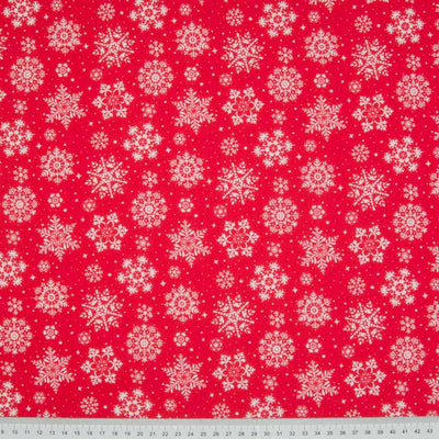 White intricate snowflakes printed on a red christmas polycotton fabric with a cm ruler at the bottom