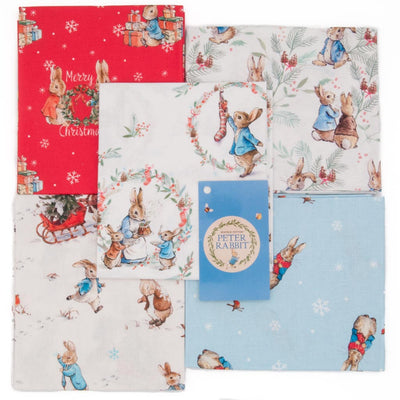 Five cotton fat quarters arranged in a square with a red, a blue and three white backgrounds and festive Peter Rabbit scenes printed on each.