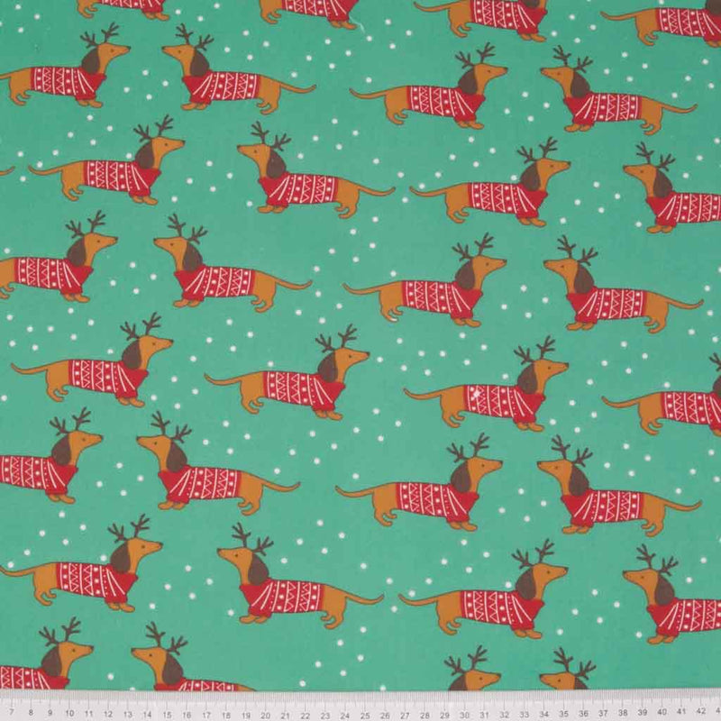 Cute little dachschunds sport reindeer antlers and christmas jumpers on this green polycotton fabric with a cm ruler at the bottom