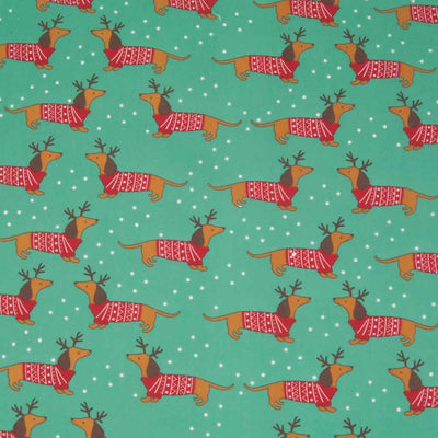 Cute little dachschunds sport reindeer antlers and christmas jumpers on this green polycotton fabric.