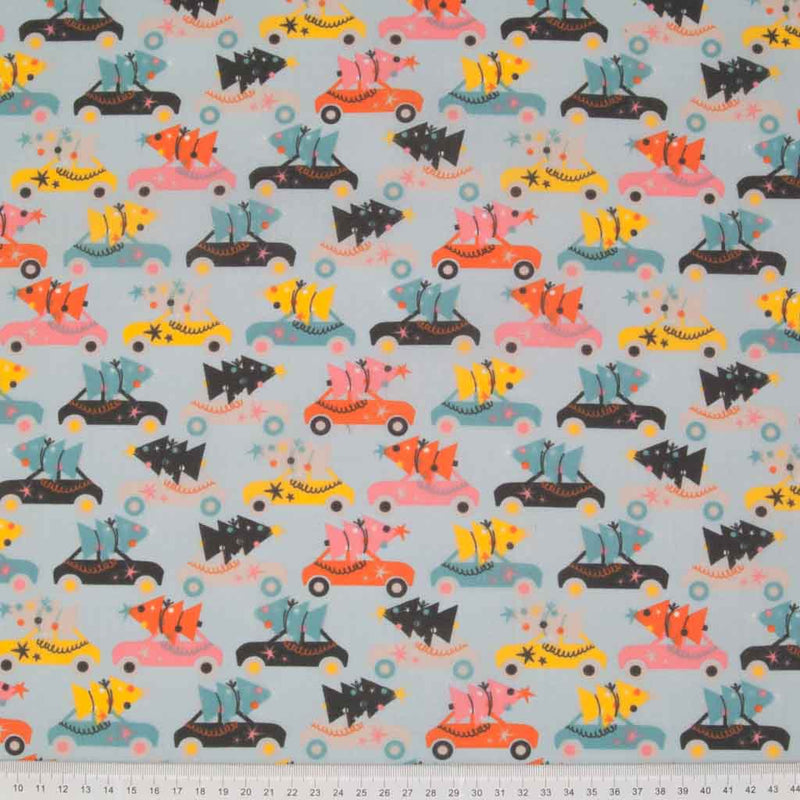 Rows of colourful cars carrying christmas trees are printed on a pale blue polycotton fabric with a cm ruler at the bottom