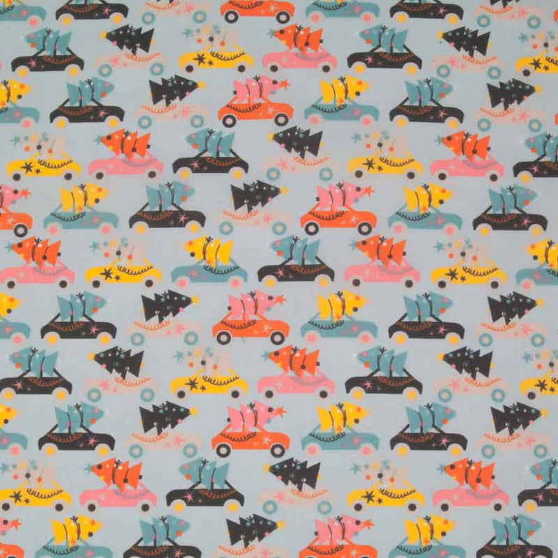 Rows of colourful cars carrying christmas trees are printed on a pale blue polycotton fabric
