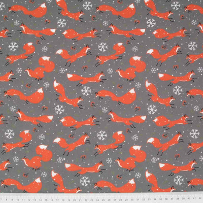 Jumping foxes, snowflakes and stars are printed on a grey polycotton fabric with a cm ruler at the bottom