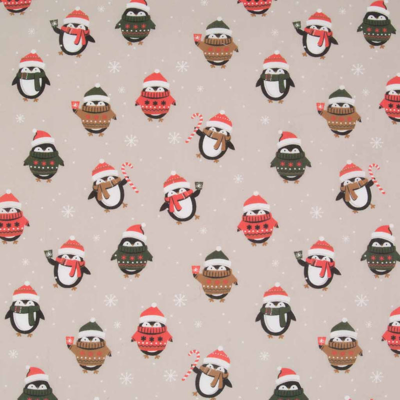 Festive penguins wearing christmas jumpers and wooly hats are printed on a beige polycotton fabric