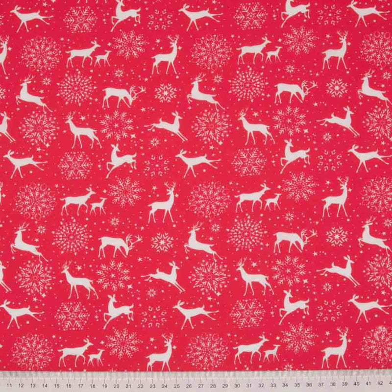 White reindeer and snowflakes are printed on a red, christmas polycotton fabric with a cm ruler at the bottom