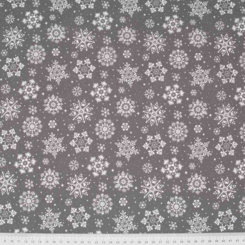 Pretty white intricate snowflakes printed on a grey polycotton fabric with a cm ruler at the bottom