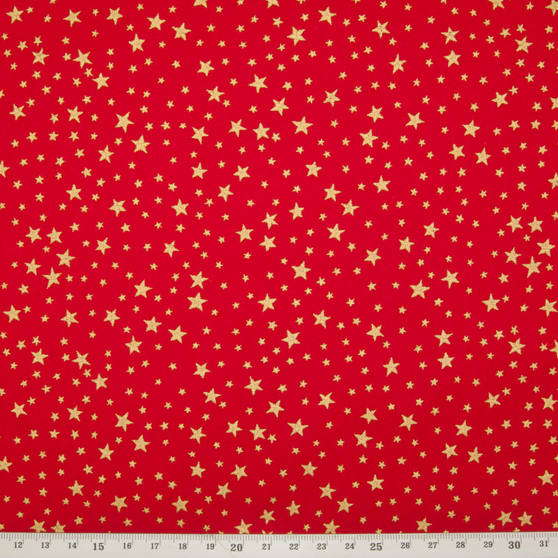 A red christmas cotton fabric featuring small metallic gold stars in a tossed pattern including ruler for perspective