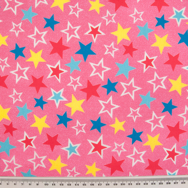Red, Yellow and Blue Stars are printed on a cotton poplin fabric by Rose & Hubble with a Pink background with ruler for size perspective