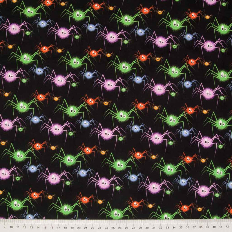 Bright purple, green and orange spiders are printed on a black 100% cotton halloween fabric with a cm ruler at the bottom