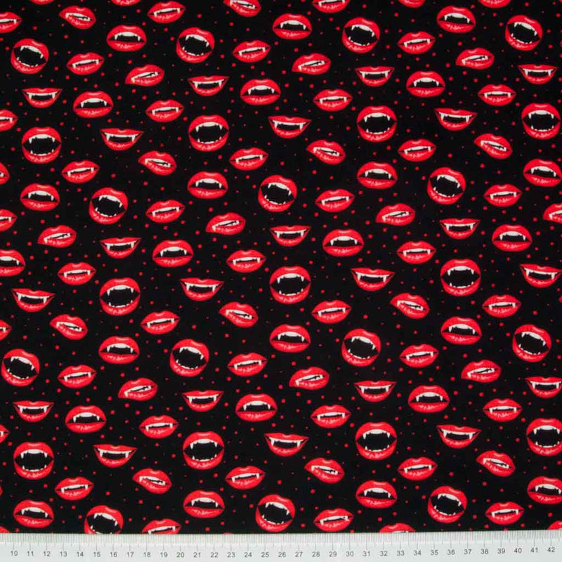 Vampire mouths with fang teeth and bright red lips are printed on a black, 100% cotton halloween fabric with a cm ruler at the bottom