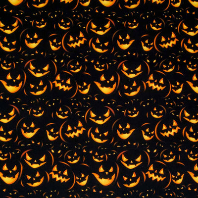 Menacing pumpkin faces in glowing orange are printed on a black 100% cotton halloween fabric