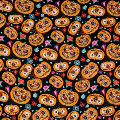 Orange halloween pumpkins with a day of the dead floral design are printed on a black, 100% cotton fabric